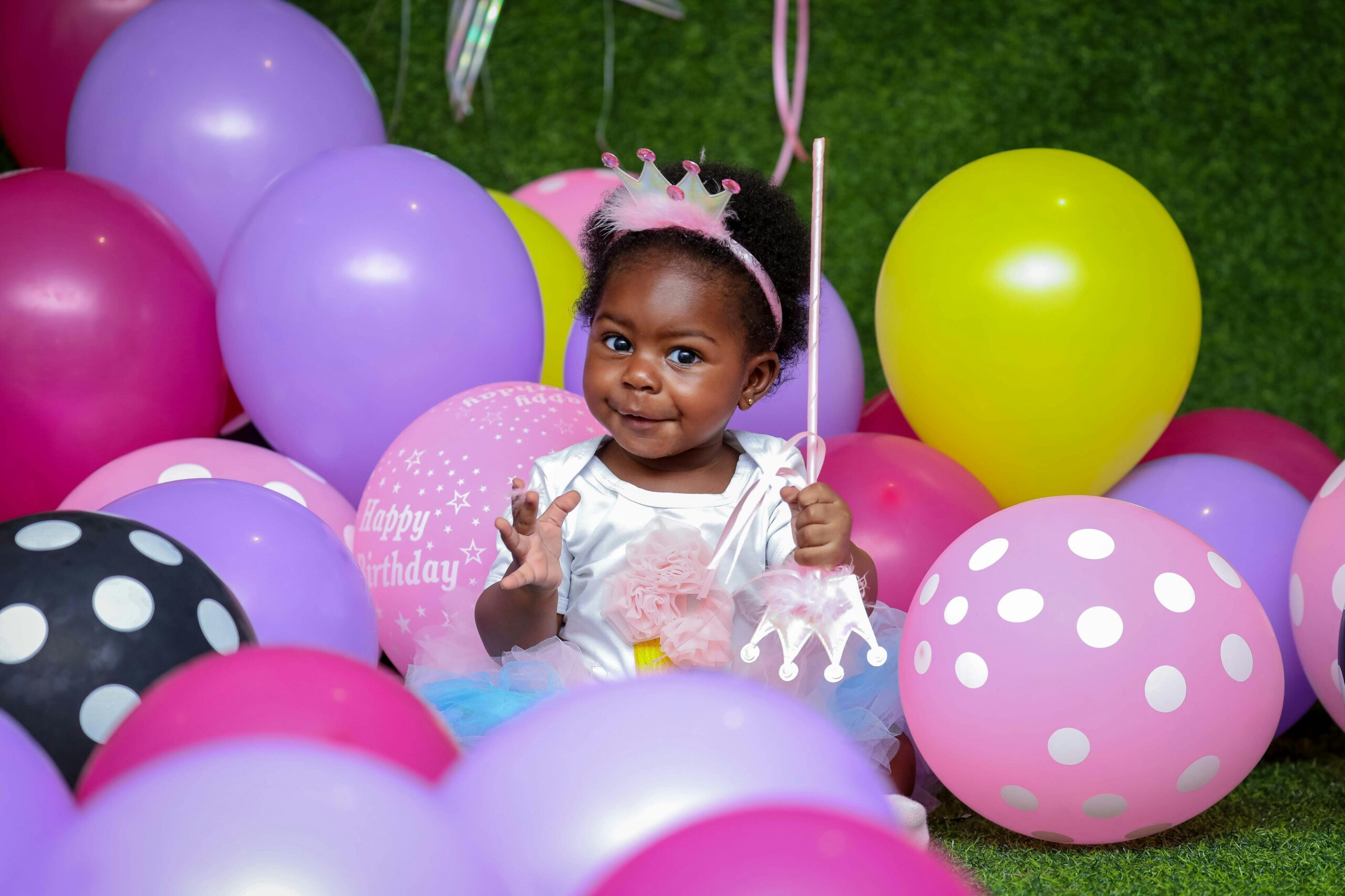 Cute child surrounded by colorful balloons enjoying a birthday party.