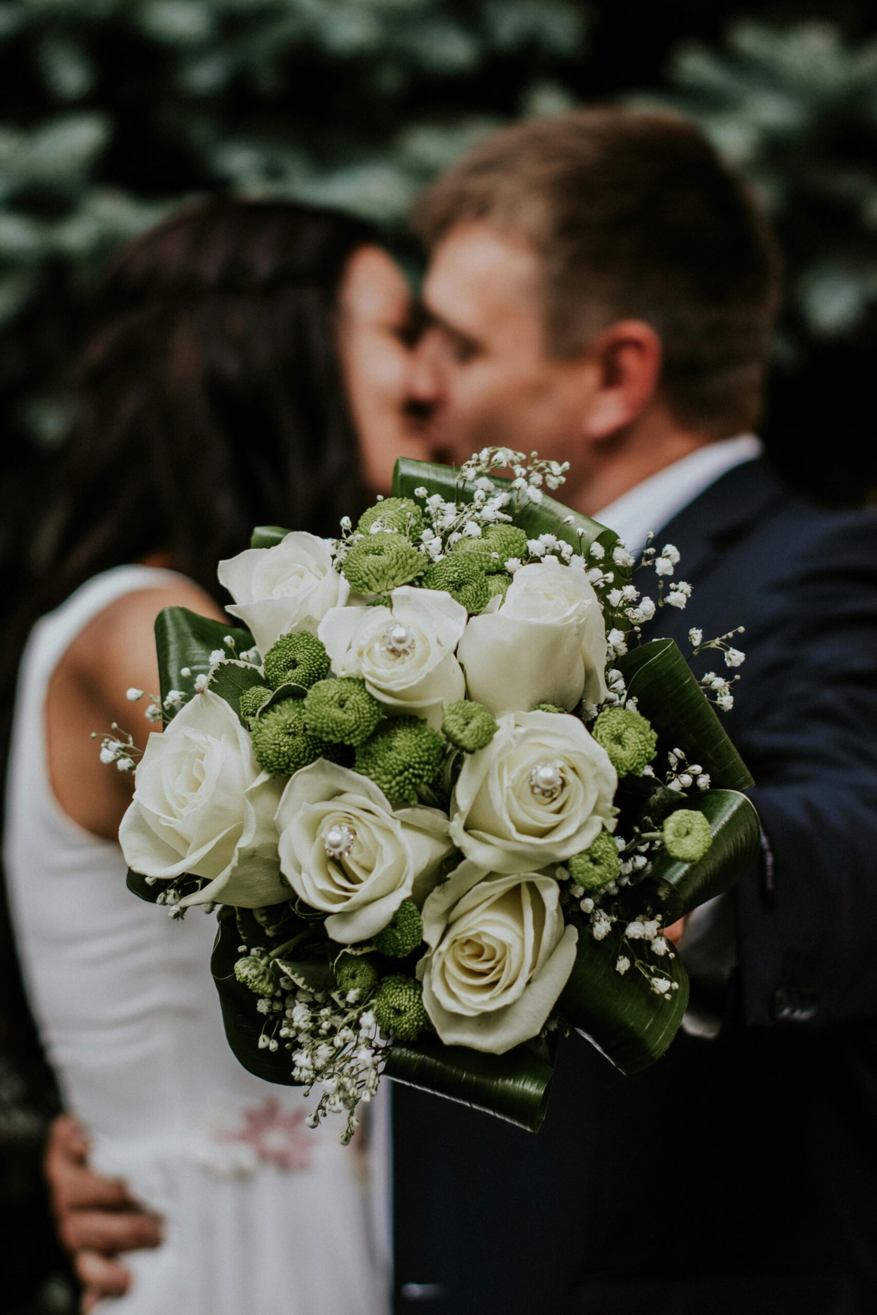 A couple embracing with a focus on a white rose and green floral wedding bouquet.